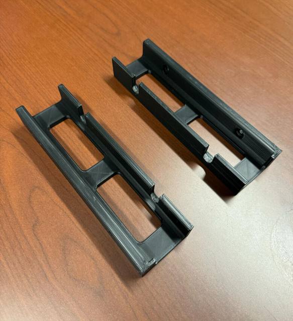 Black 3D printed bracket on a wooden shelf